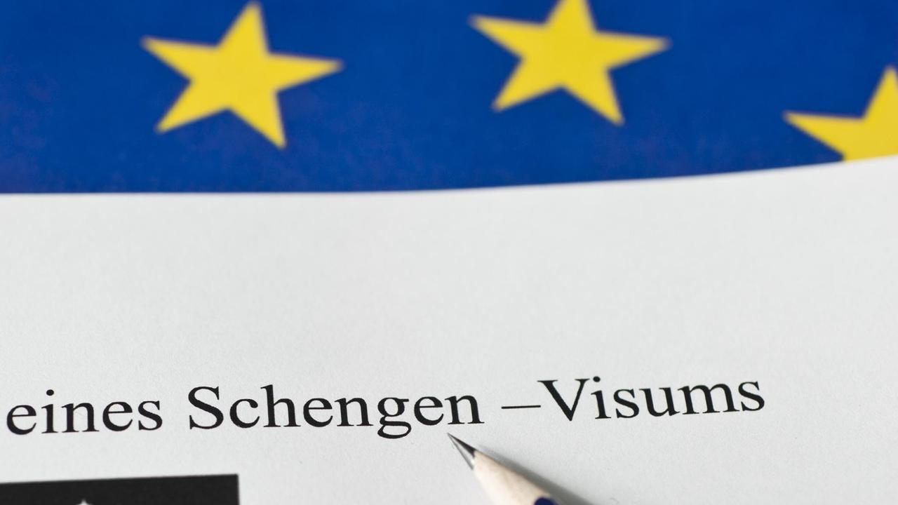 Ein Antrag auf Erteilung eines Schengen-Visums liegt auf einem Tisch vor einer EU-Flagge