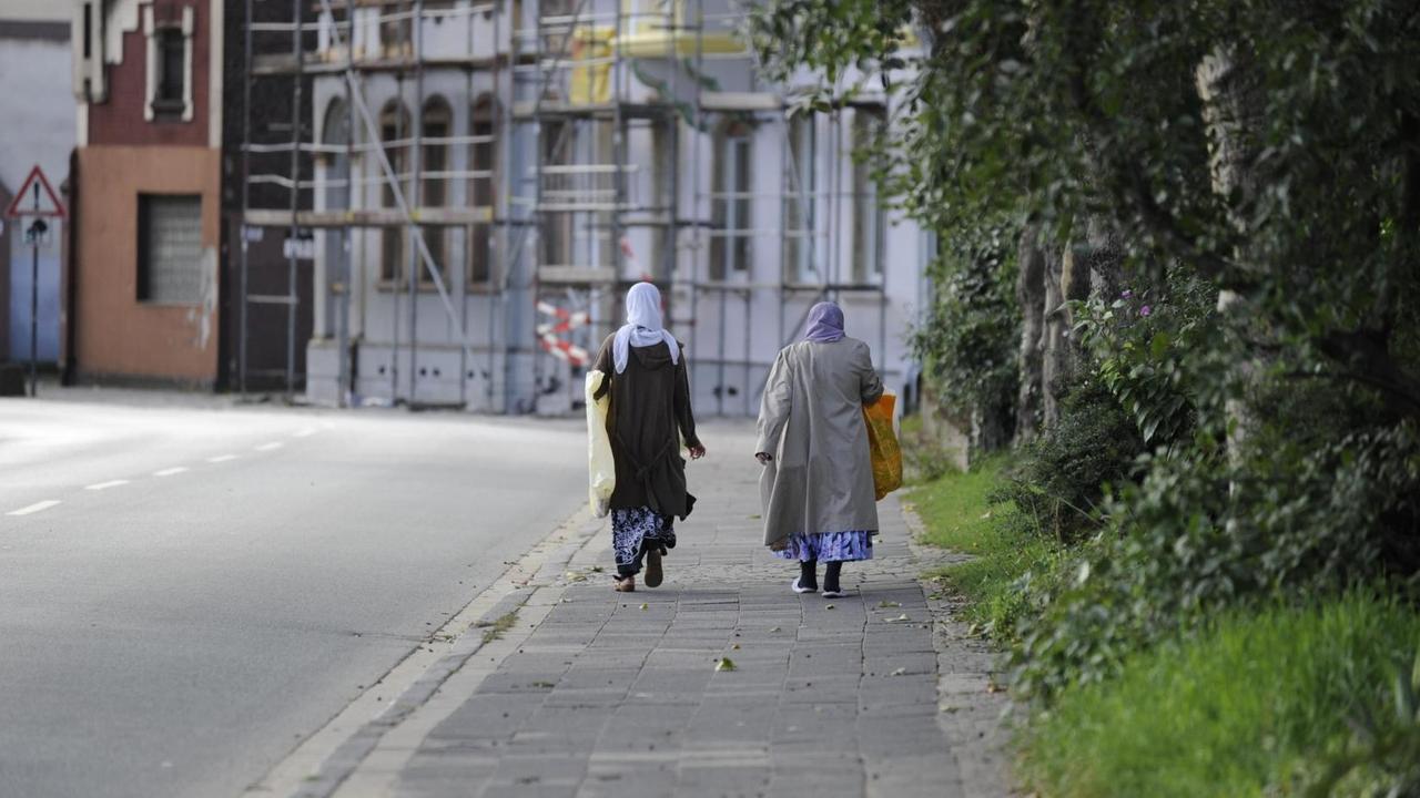 Das Bild zeigt zwei muslimische Frauen in weiterer Distanz auf einem Gehweg entlang laufen.
