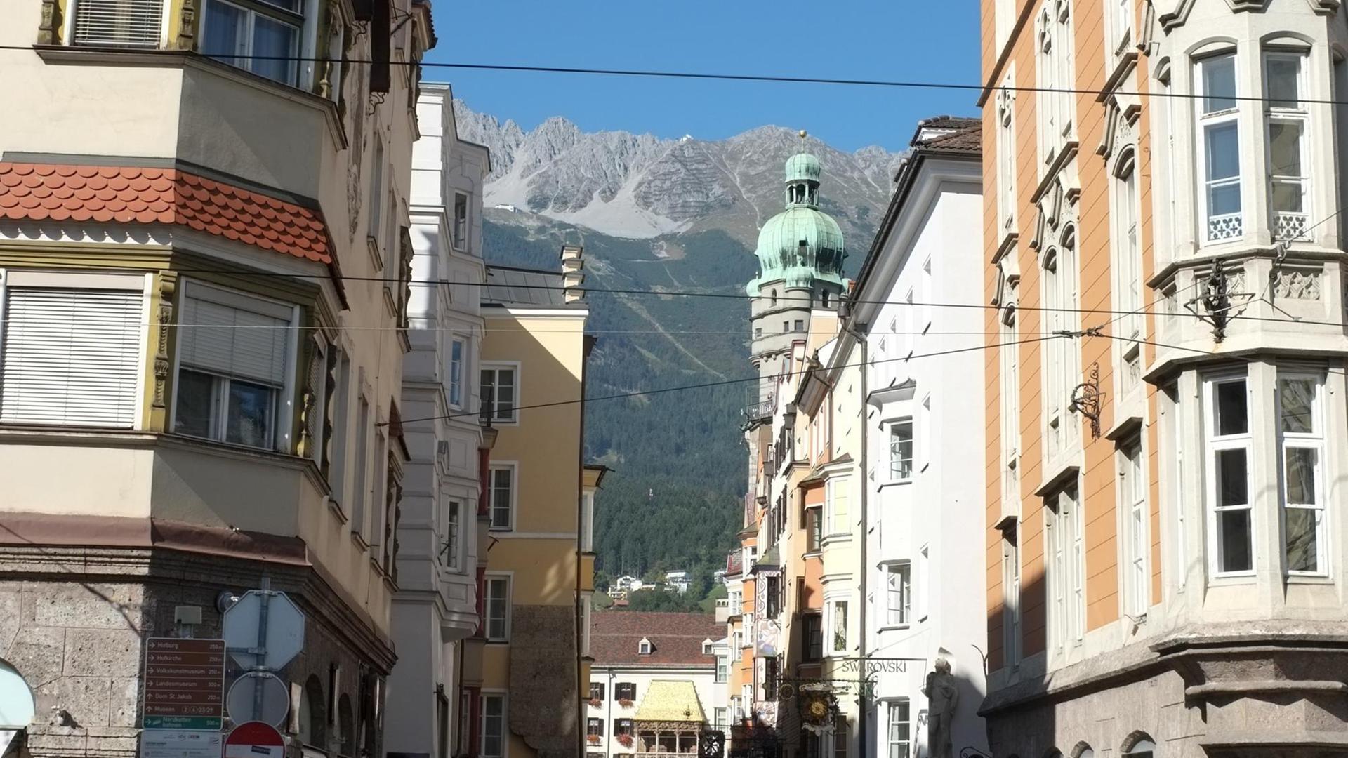 Blick in eine Altstadtgasse Innsbrucks mit den Alpen im Hintergrund und dem "Goldenen Dachl" davor. Das Goldene Dachl ist ein Gebäude mit spätgotischem Prunkerker in der Innsbrucker Altstadt und gilt als Wahrzeichen der Stadt