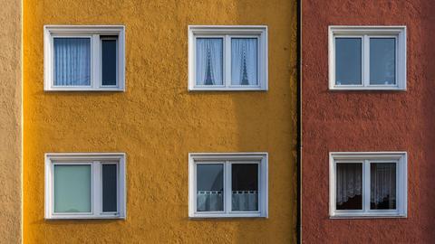Bildausschnitt der Fassade zweier nebeneinanderstehender Mehrfamilienhäuser: das eine Haus ist ockergelb gestrichen, das andere rot.