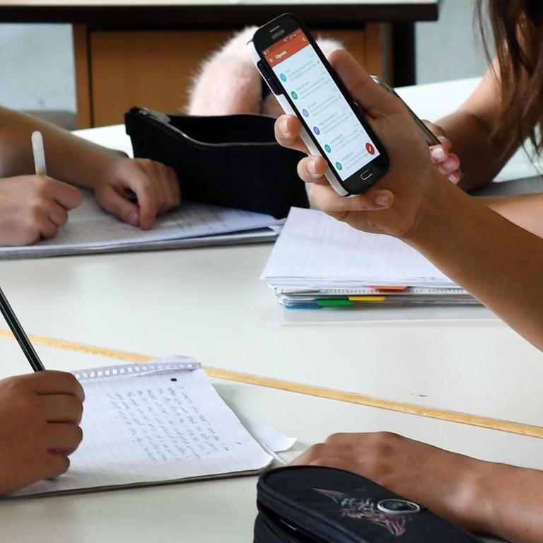 Schüler hält im Unterricht ein Handy in den Händen 