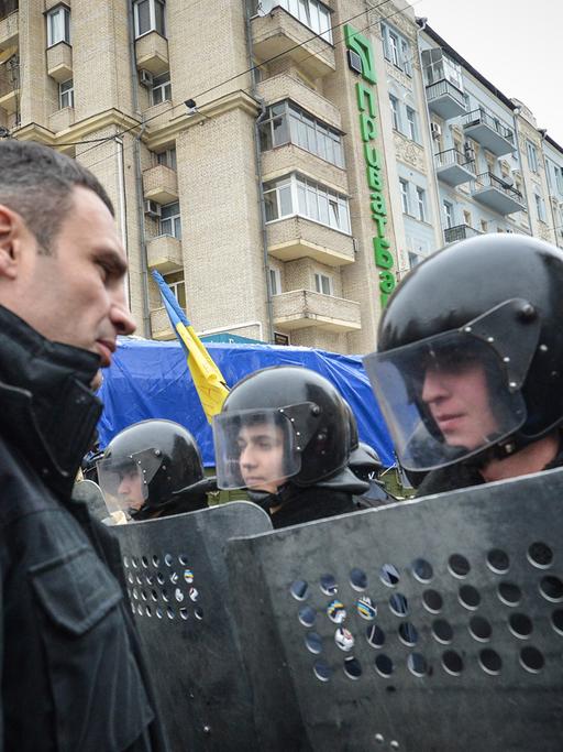 Vitali Klitschko spricht mit einem Polizisten, der mit Helm und Schild ausgerüstet ist.