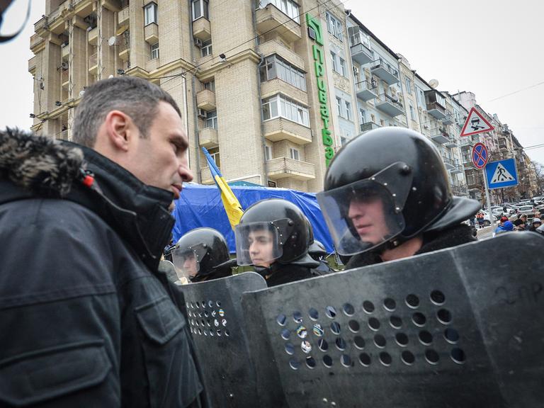Vitali Klitschko spricht mit einem Polizisten, der mit Helm und Schild ausgerüstet ist.