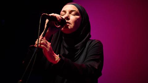 Die Sängerin und Komponistin Sinead O'Connor vor lila Hintergrund, Sie trägt einen Schleier und ein dunkles Oberteil.