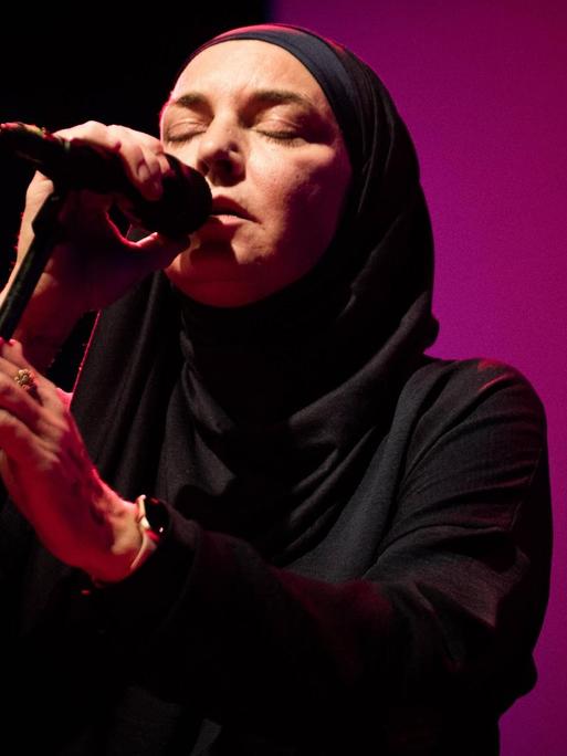 Die Sängerin und Komponistin Sinead O'Connor vor lila Hintergrund, Sie trägt einen Schleier und ein dunkles Oberteil.