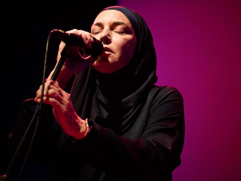 Die Sängerin und Komponistin Sinead O'Connor vor lila Hintergrund, Sie trägt einen Schleier und ein dunkles Oberteil.