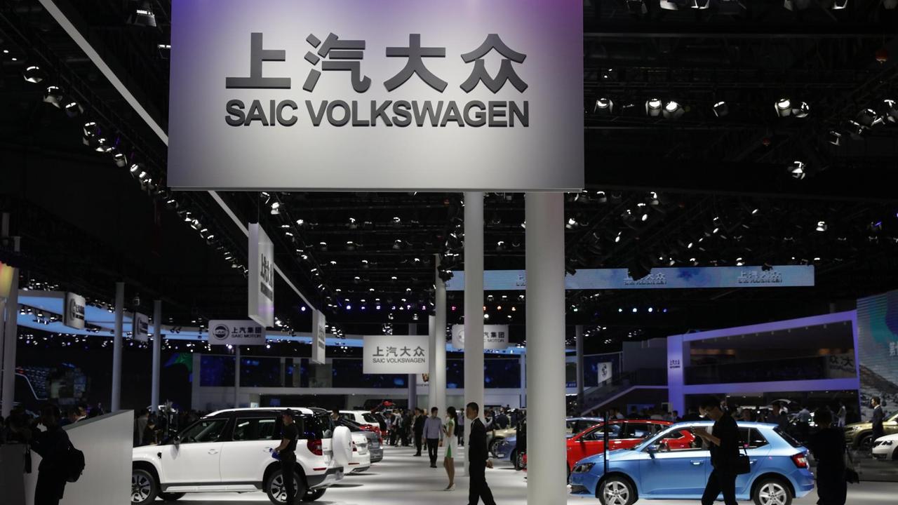 Autos stehen in einer Halle auf der Internationalen Automobil-Ausstellung. Menschen gehen unter einem Schild mit der Aufschrift "Volkswagen" lang.