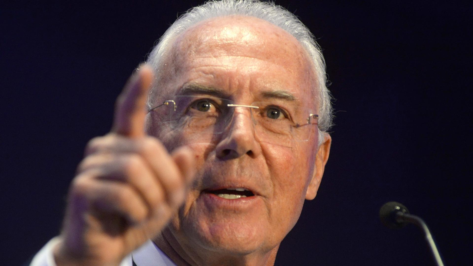 Franz Beckenbauer hebt während einer Rede die rechte Hand und zeigt mit dem Finger auf etwas.