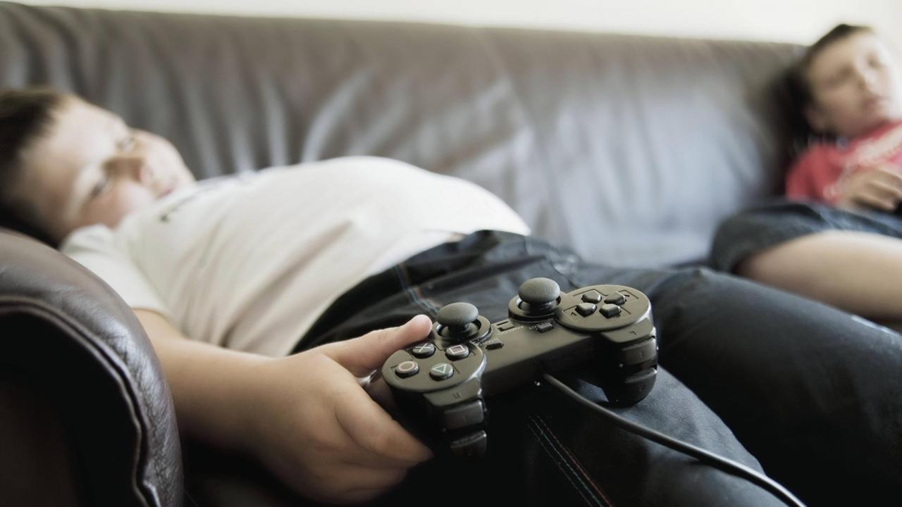 Zwei schlafende Jungs mit Game-Controllern schlafen auf einem Sofa.