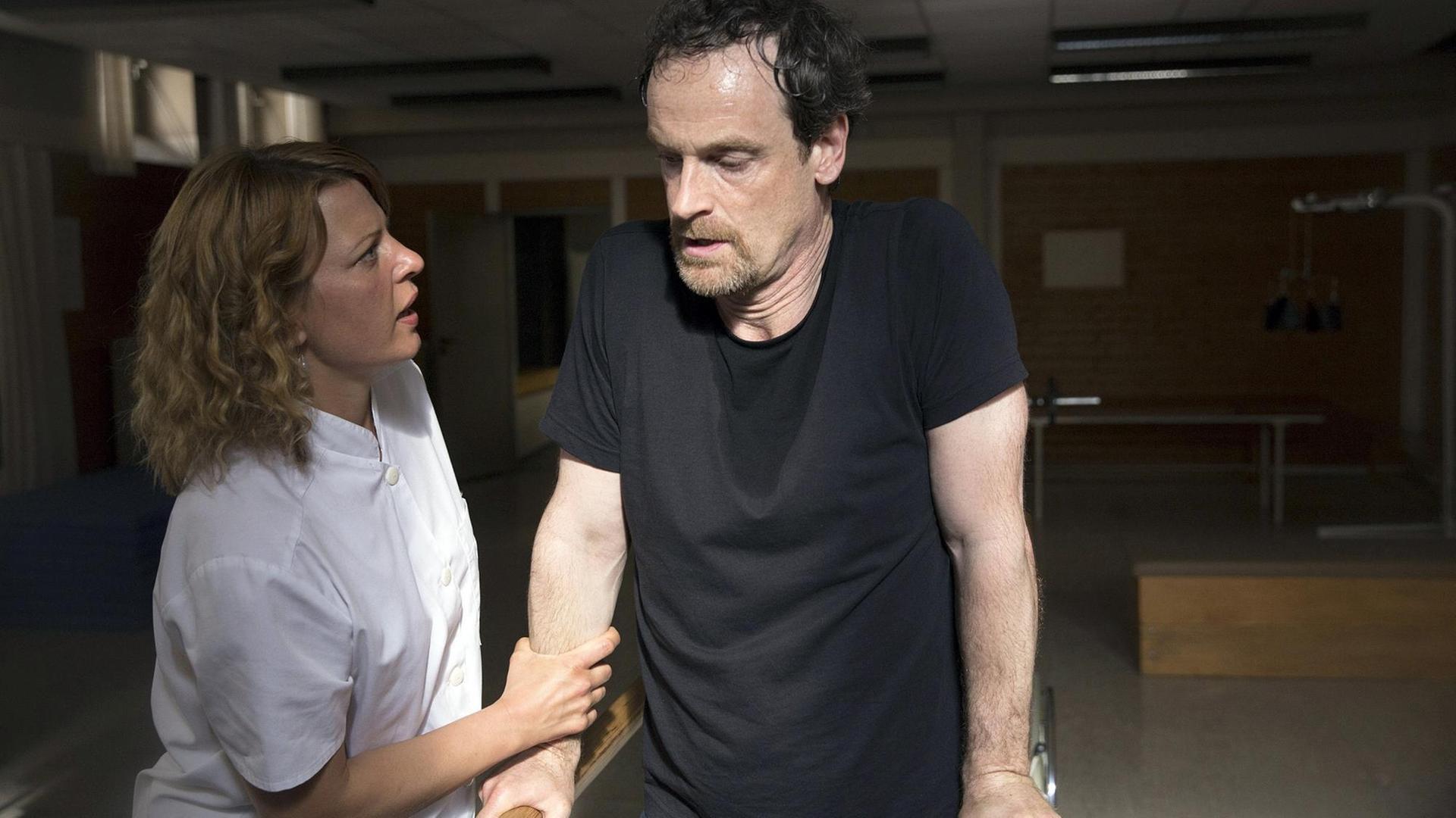 Szene aus der 4. Staffel der Serie "Weissensee": Petra Zeiler (Jördis Triebel) ist beeindruckt vom Kampfgeist ihres Patienten Falk (Jörg Hartmann). Beide stehen an einem Barren.