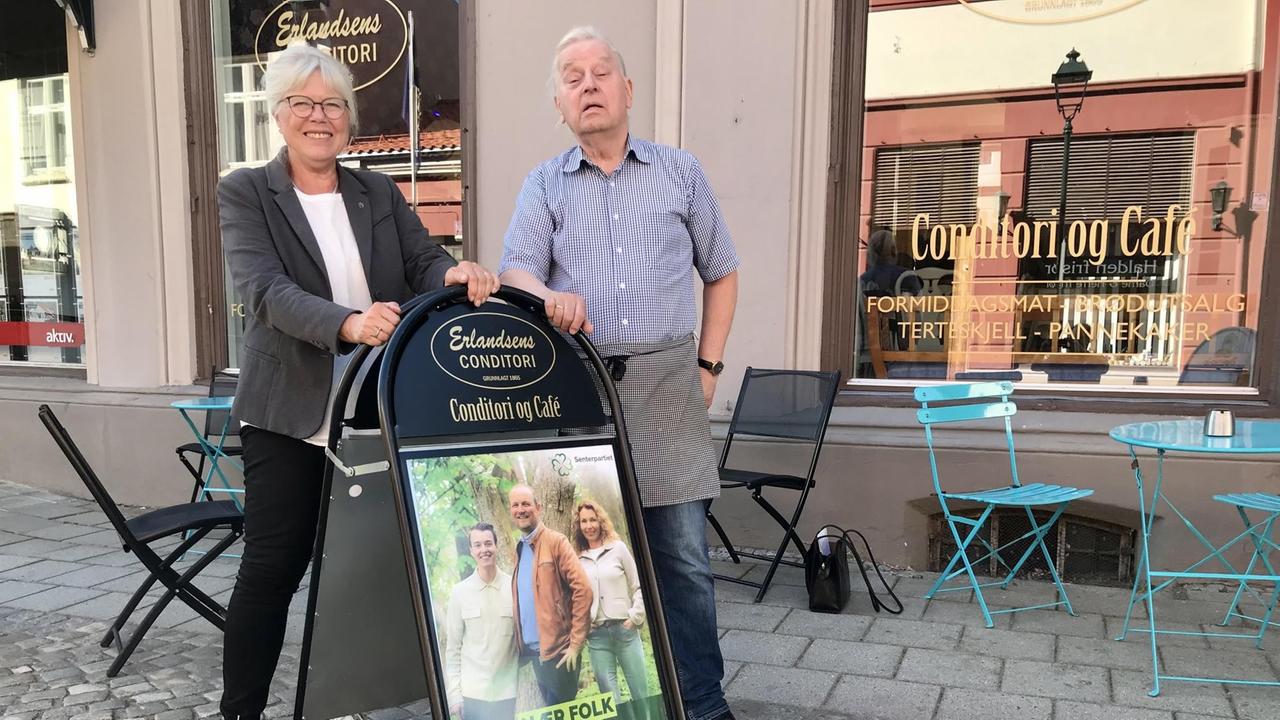 Mann und Frau stehen vor einem Kaffee in der Fußgängerzone. Sie lehnen sich an an eine Werbetafel.