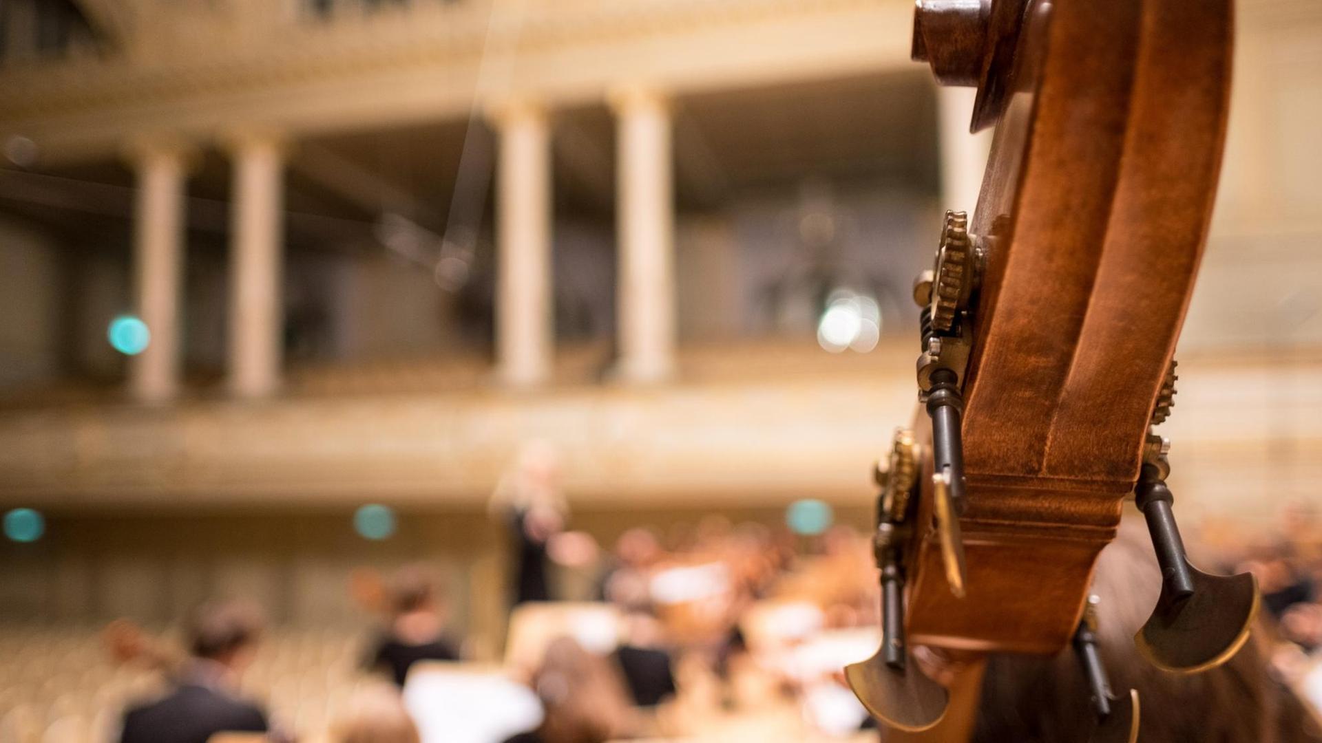 Ein Orchester probt in einem Konzertsaal. Im Vordergrund: Ein Streichinstrument.