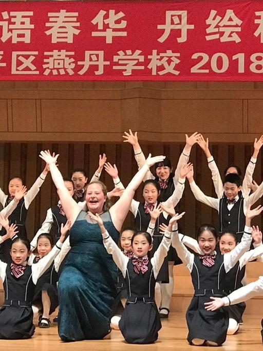 Mädchen undgs knien mit ausgestreckten Armen in Chorformation auf einer Bühne.