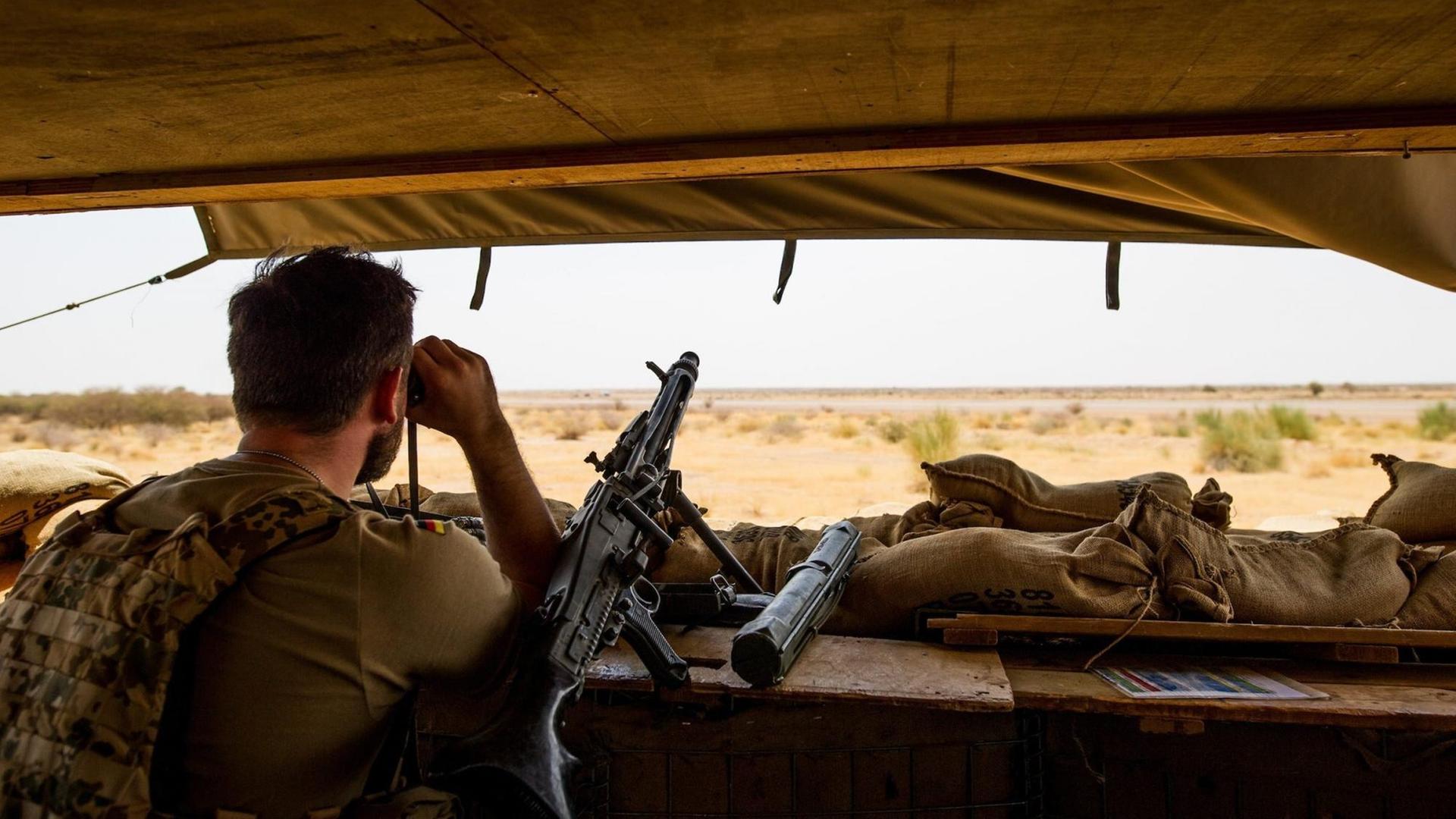 Ein Bundeswehrsoldat schaut mit einem Fernglas ins Gelände.