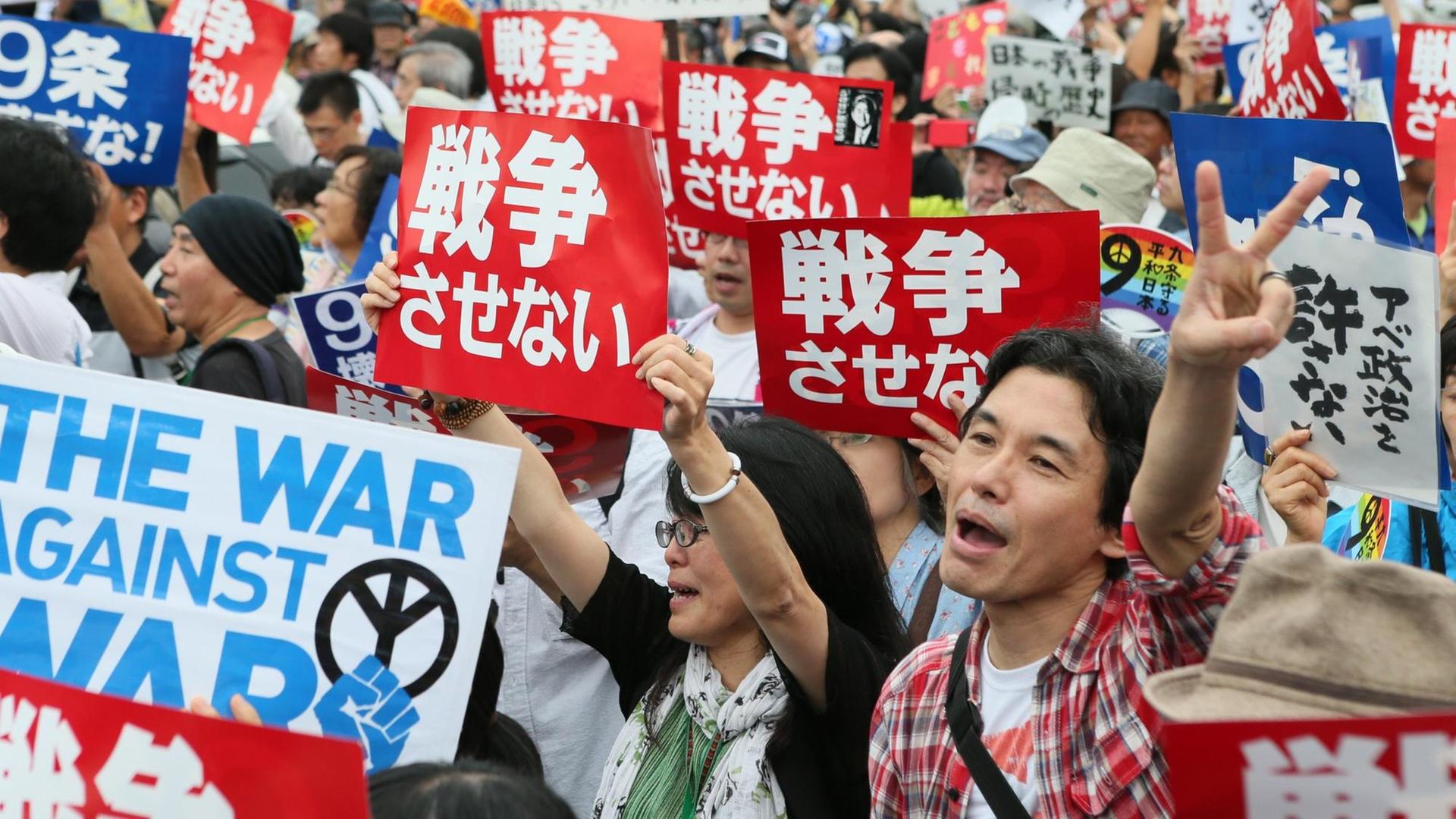 Man sieht viele Menschen. Sie halten Plakate in japanischer Schrift hoch. Sie protestieren gegen die Regierung. Man sieht viele Menschen. Sie halten Plakate in japanischer Schrift hoch. Sie protestieren gegen die Regierung.