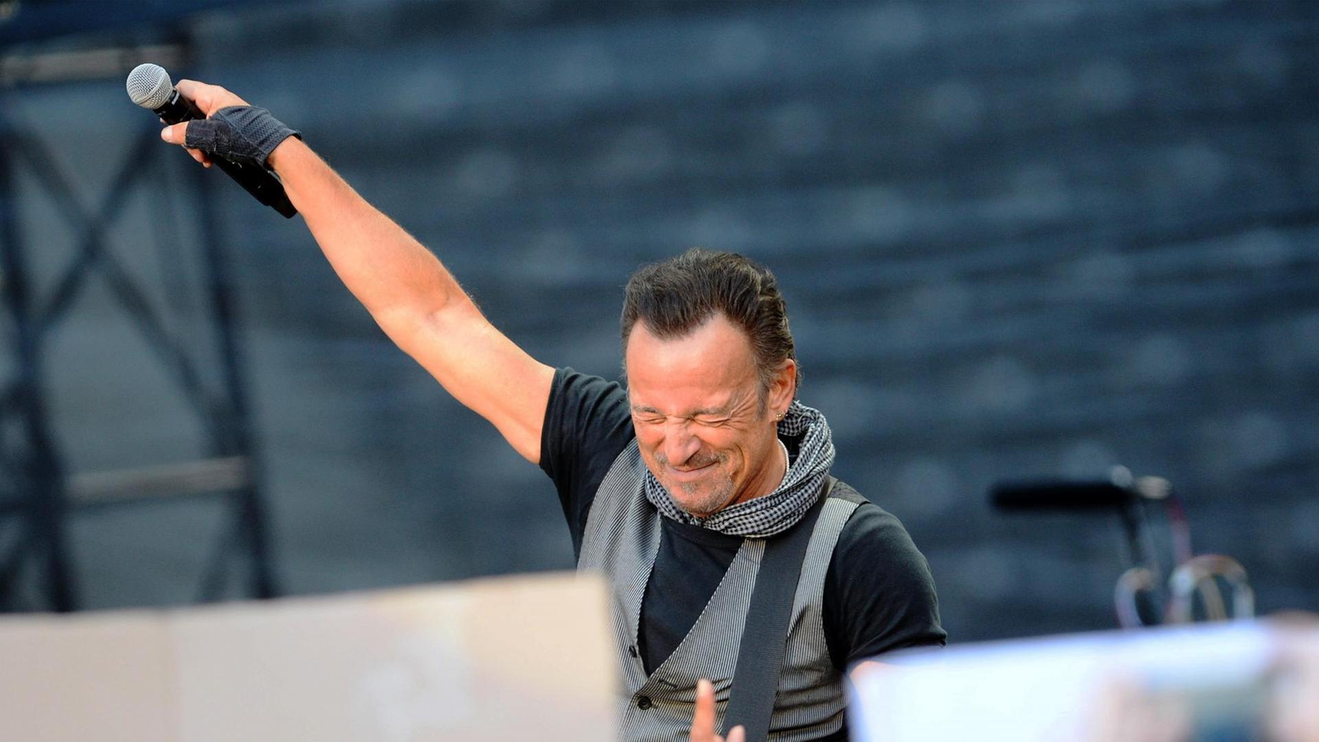 Der US-Rockstar Bruce Springsteen steht auf einer Bühne mit gesclossenen Augen und hält ein Mikrofon Richtung Publikum