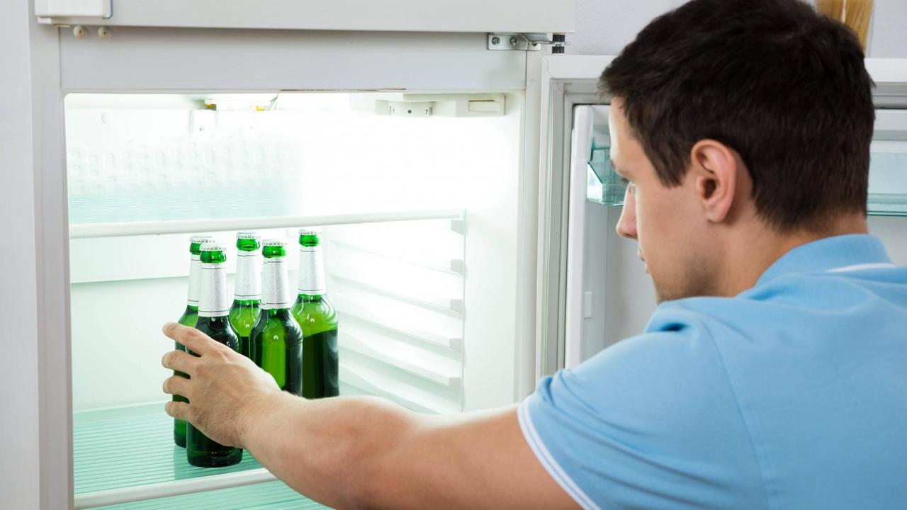 Ein junger Mann nimmt eine Bierflasche aus dem Kühlschrank.
