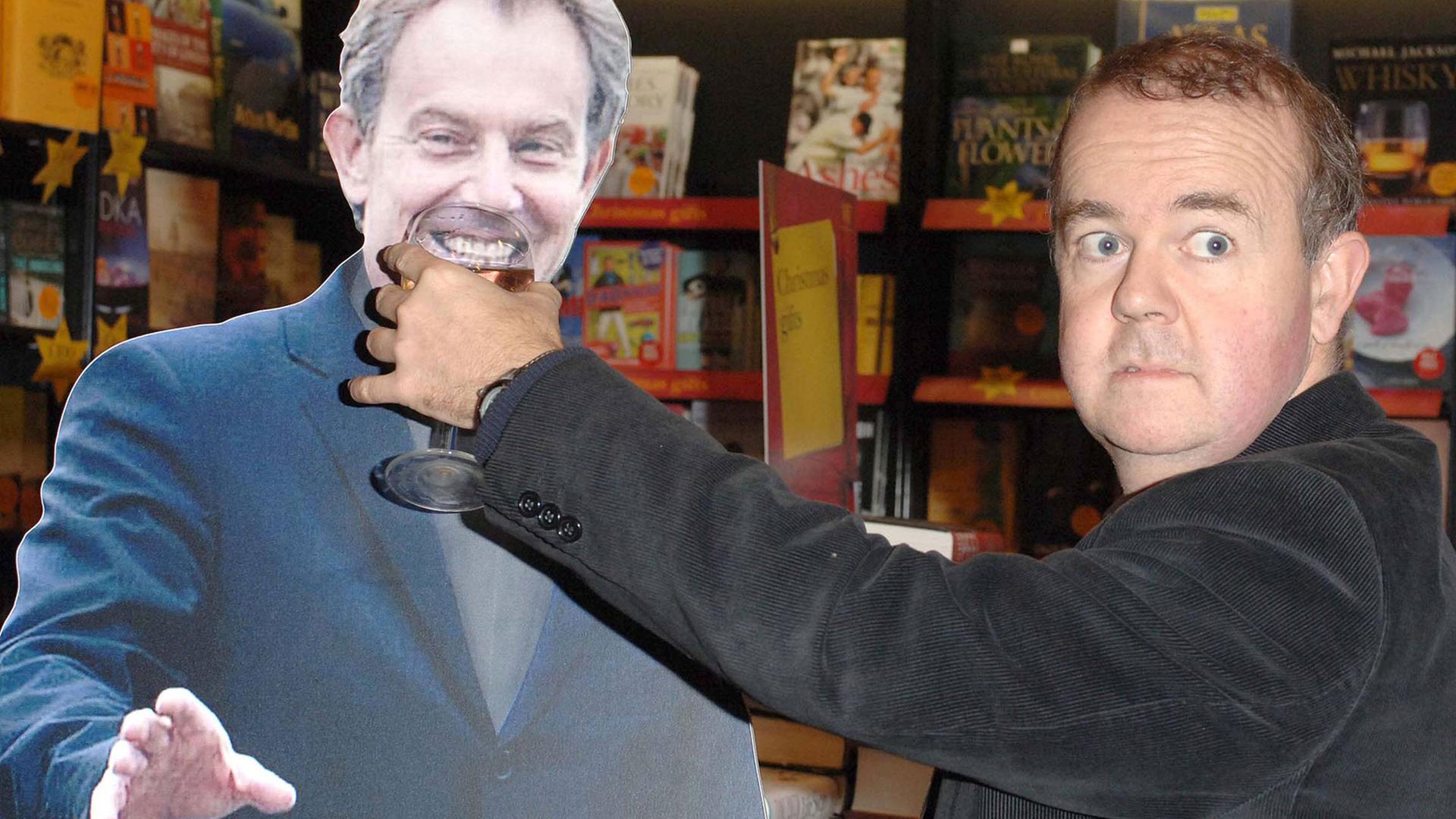 Der britische Komiker Ian Hislop hält bei einer Signierstunde für sein Buch "Private Eye Annual 2005" in London einer Pappfigur des britischen Premierministers Tony Blair ein Weinglas an den Mund und grinst.