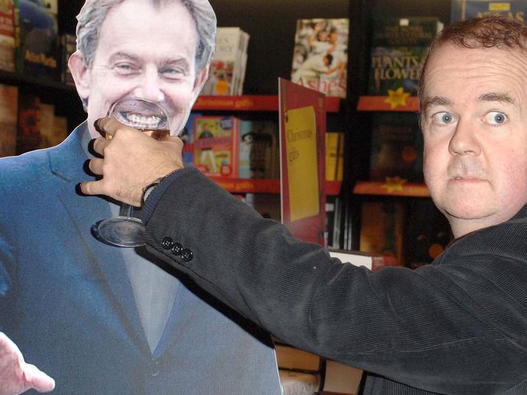 Der britische Komiker Ian Hislop hält bei einer Signierstunde für sein Buch "Private Eye Annual 2005" in London einer Pappfigur des britischen Premierministers Tony Blair ein Weinglas an den Mund und grinst.