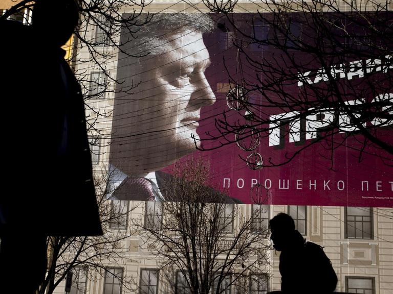 Fußgänger gehen an einem Plakat von Petro Poroschenko an einer Hauswand vorbei.