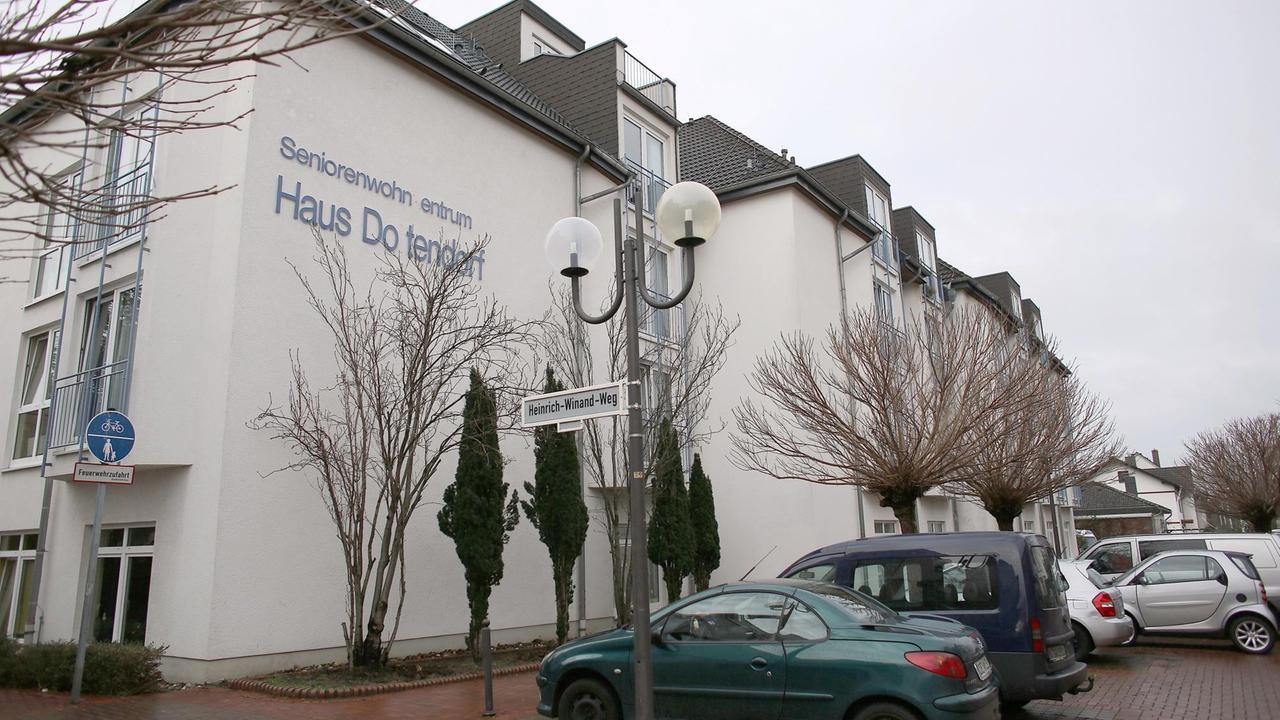Ein weißes Gebäude mit der Aufschrift "Seniorenwohnzentrum Haus Dottendorf", im Vordergrund parkende Autos.