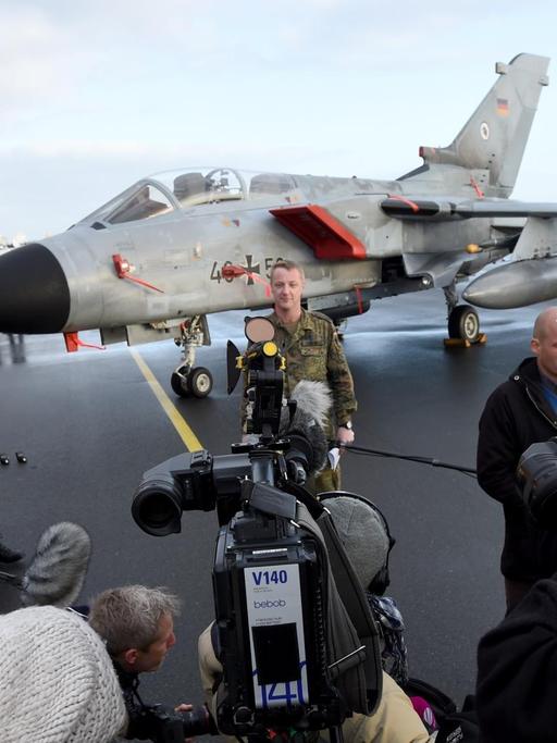 Zu sehen ist im Hintergrund ein Tornado-Kampfjet, davor stehen Journalisten mit Kameras und ein Bundeswehr-Soldat.