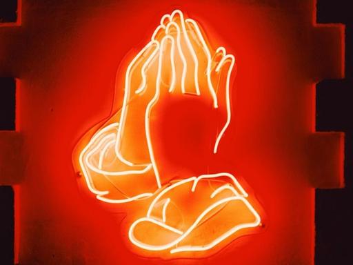 Ein rot leuchtendes Neonschild betender Hände.