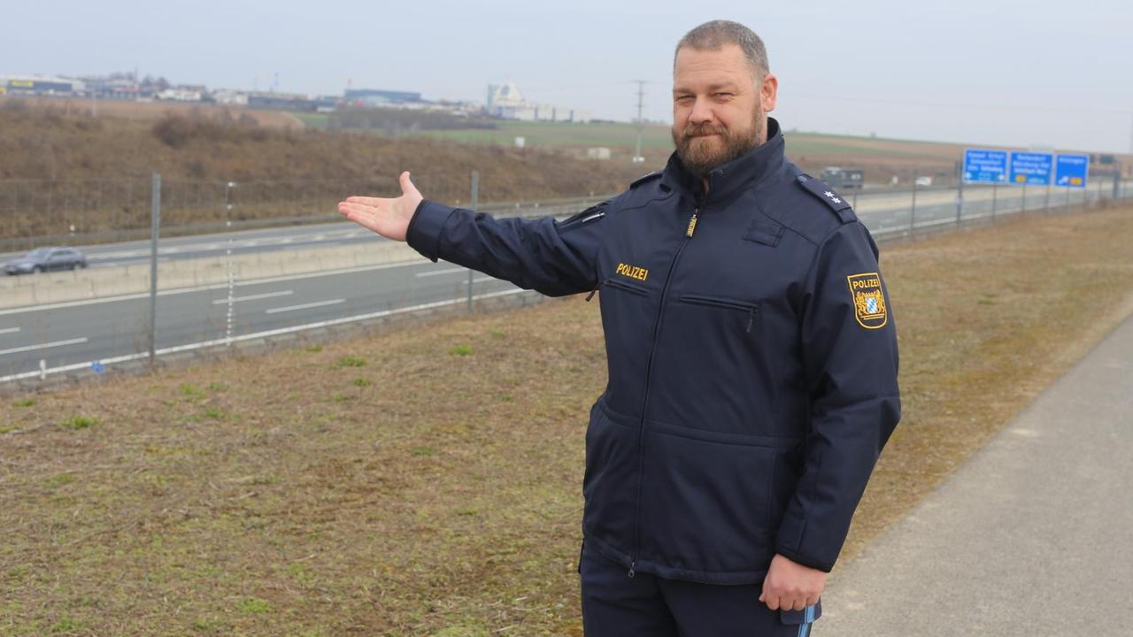 Ein Mann in Polizeiuniform steht an einer Autobahn.