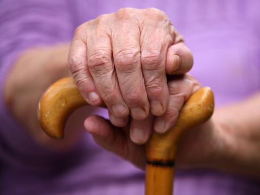 Eine Seniorin sitzt in Leichlingen mit einem Gehstock auf einer Parkbank.