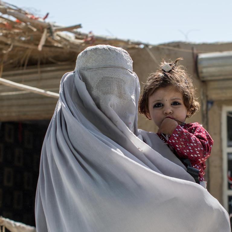 Am Stadtrand von Kandahar ist eine verhüllte Bettlerin mit ihrem Kind zu sehen, die auf Spenden aus den vorbei fahrenden Autos hofft.