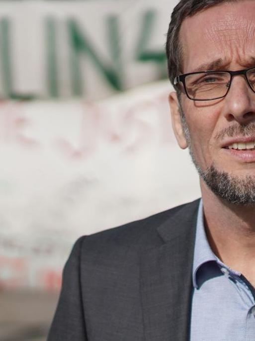 Ein Mann steht auf einem Platz, im Hintergrund sind Menschen und Transparente zu sehen. Der Mann im Vordergrund ist Volker Quaschning, Professor für regenerative Energiesysteme, er schaut in die Kamera.