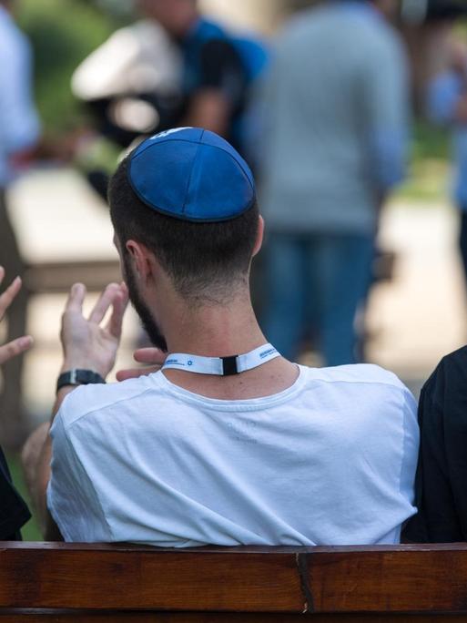Symbolbild: Zwei junge Muslima mit Kopftuch und ein junger jüdischer Mann mit Kippa unterhalten sich miteinander. Sie befinden sich in der KZ-Gedenkstätte Auschwitz.