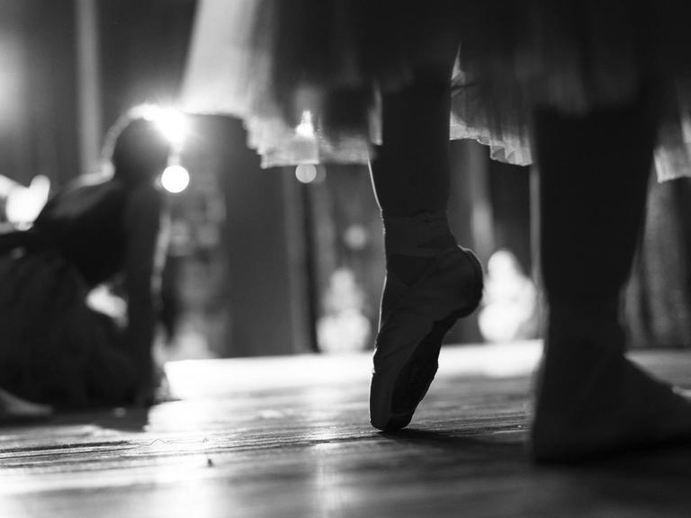 Die Schwarz-Weiß-Aufnahme zeigt Beine einer Frau mit Ballettschuhen.