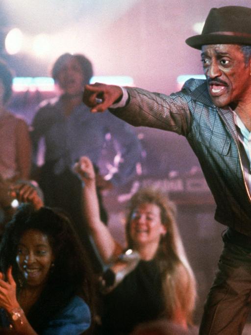 Der amerikanische Allround-Entertainer Sammy Davis Jr. steht bei Dreharbeiten auf einer Bühne, Fans jubeln ihm zu.