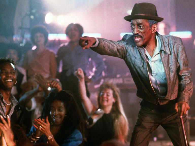 Der amerikanische Allround-Entertainer Sammy Davis Jr. steht bei Dreharbeiten auf einer Bühne, Fans jubeln ihm zu.