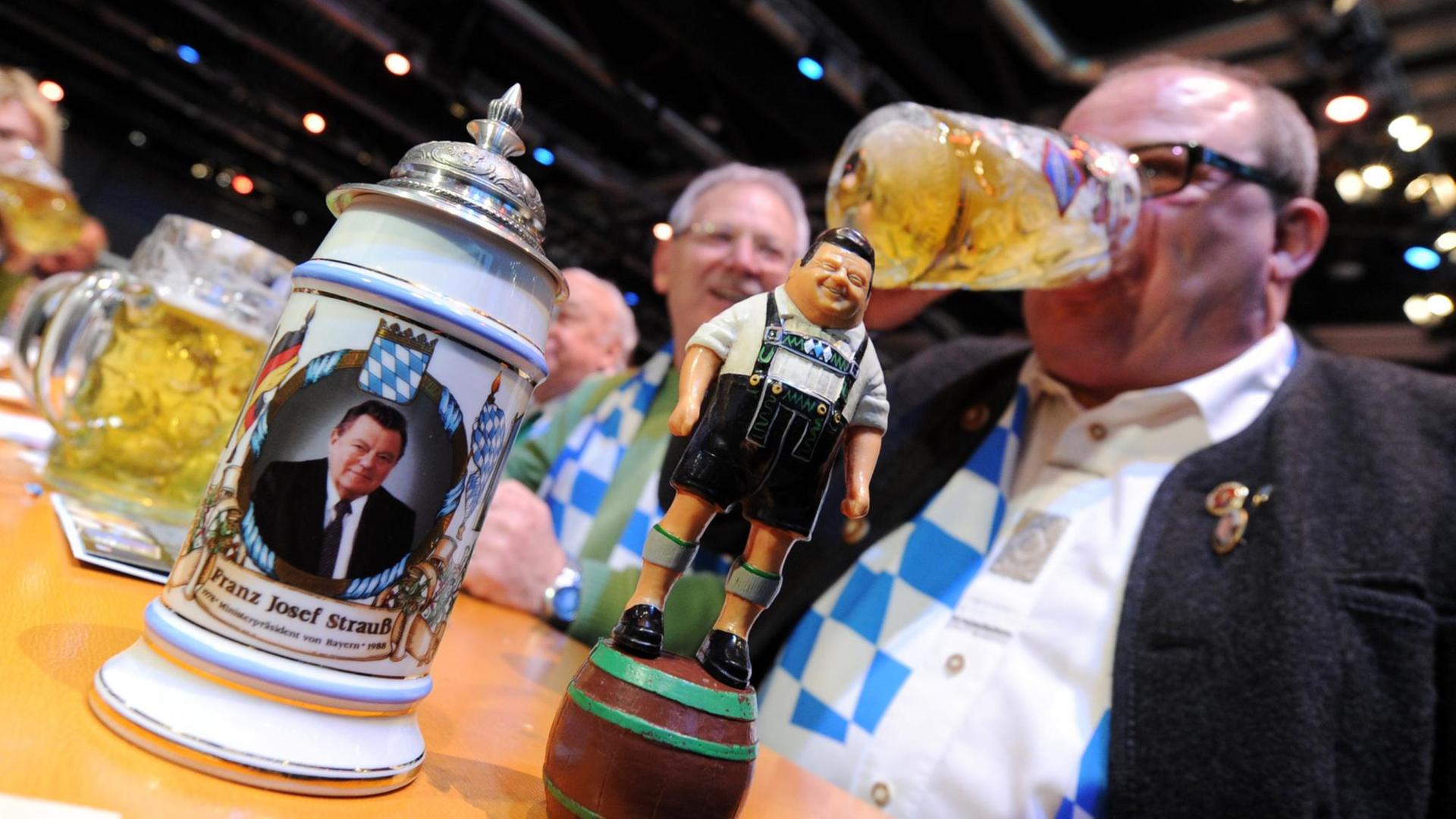 Auf einem Tisch haben Besucher des Politischen Aschermittwochs der CSU in Passau eine Figur und einen Bierkrug abgestellt, auf denen der ehemalige CSU-Vorsitzende Franz-Josef Strauß dargestellt ist.