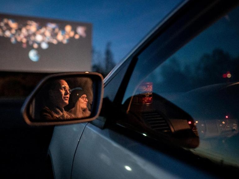 Zwei Besucher des Autokino sitzen im Auto und gucken auf die Leinwand. Das Kino in Essen hat auch während der Corona-Pandemie geöffnet.