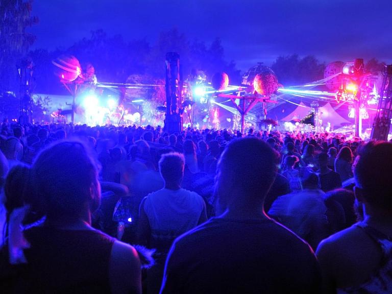 Besucher tanzen nachts auf dem bunt beleuchteten Gelände des Fusion-Festivals.