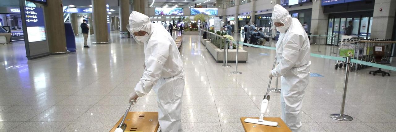 Mitarbeiter in Schutzkleidung desinfizieren Bänke in der Ankunftshalle des Flughafens 