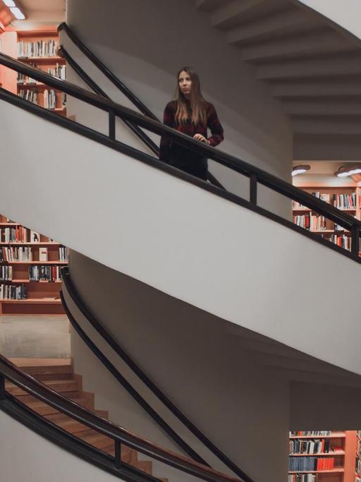 Eine junge Frau steht auf einer Treppe in einer Bibliothek.