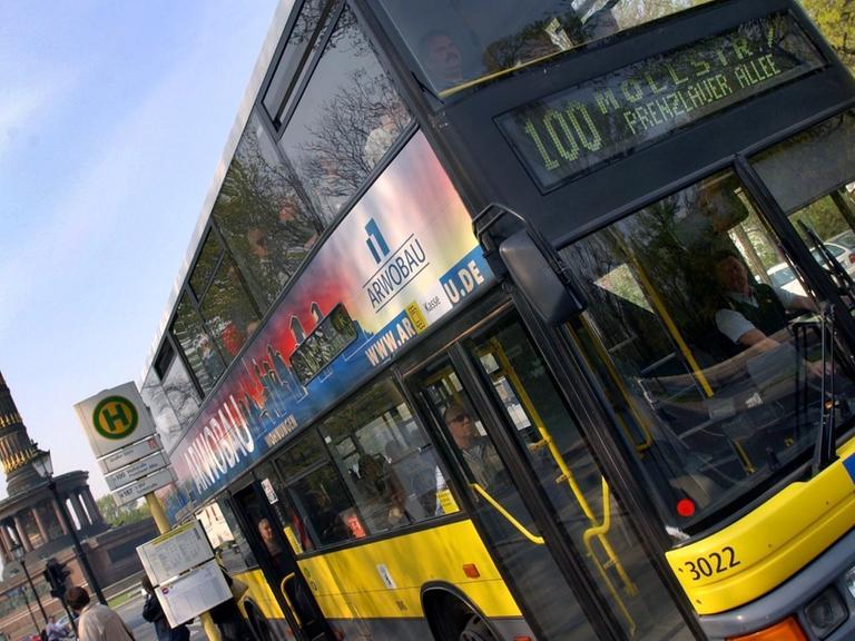 Auf dem Foto ist ein gelber Doppeldecker-Bus der Linie 100 zu sehen. Er verbindet den Westen mit dem Osten Berlins. Im Hintergrund ist die Siegessäule zu sehen.