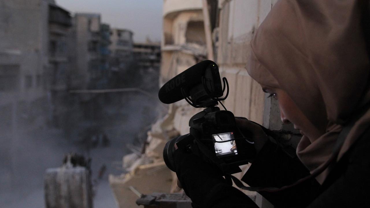 Filmszene aus "For Sama" aus der Reihe "Spotlight" beim Arabischen Filmfestival. Eine junge Frau mit Kopftuch filmt aus einem Fenster eine zerstörte Straße.