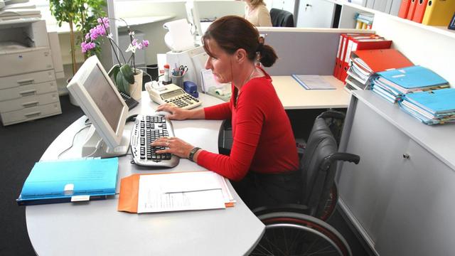 Eine Frau im Rollstuhl arbeitet am Computer im Büro.