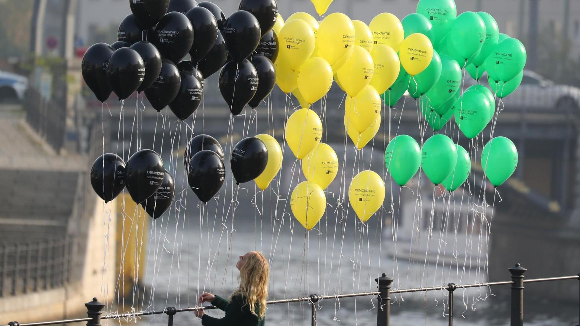 Eine junge Frau befestigt in Berlin Luftballons in den Jamaika-Farben an einem Geländer bei der Parlamentarischen Gesellschaft an der Spree.
