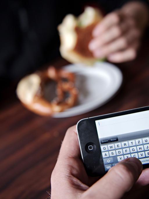 Ein Mann surft mit seinem Smartphone im Internet. Fast neun von zehn Deutschen finden es unhöflich, wenn ihr Gegenüber beim Essen immer wieder auf das Smartphone schaut. Foto: Nicolas Armer
