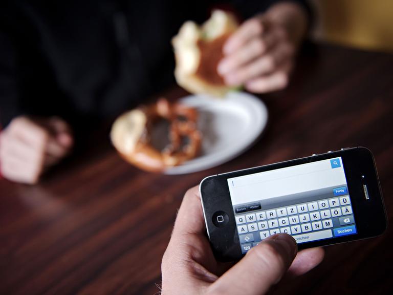Ein Mann surft mit seinem Smartphone im Internet. Fast neun von zehn Deutschen finden es unhöflich, wenn ihr Gegenüber beim Essen immer wieder auf das Smartphone schaut. Foto: Nicolas Armer