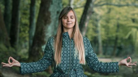 Eine Frau mit ausgebreiteten Armen beim Meditieren im Wald