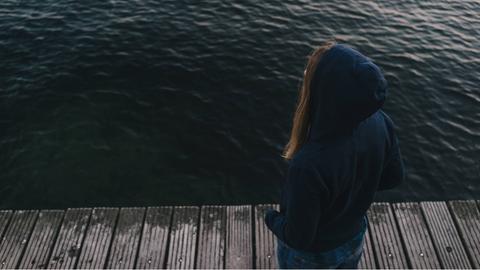 Eine junge Frau auf einem Steg blickt ins Wasser