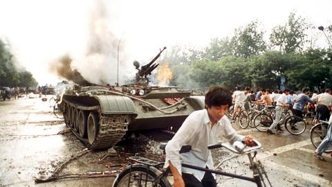 Menschen mit Fahrrädern neben einem in Brand gesetzten Panzer westlich des Tien An Men-Platzes in Peking (Foto vom 4.6.1989). Chinesisches Militär hatte am 4.6.1989 auf dem Platz des Himmlischen Friedens (Tien An Men) in Peking, auf dem Studenten für mehr Demokratie, Pressefreiheit und gegen Parteiprivilegien demonstrierten, ein Blutbad angerichtet.