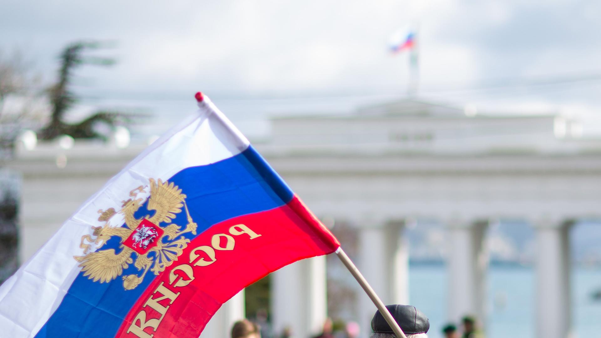 Ein Mann mit einer Russland-Flagge geht auf ein staatliches Gebäude mit Säulen zu